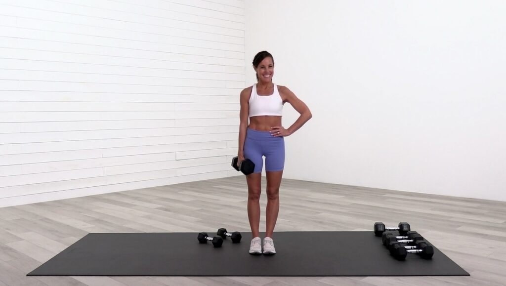 Women in her 40s standing in white workout room with dumbbells